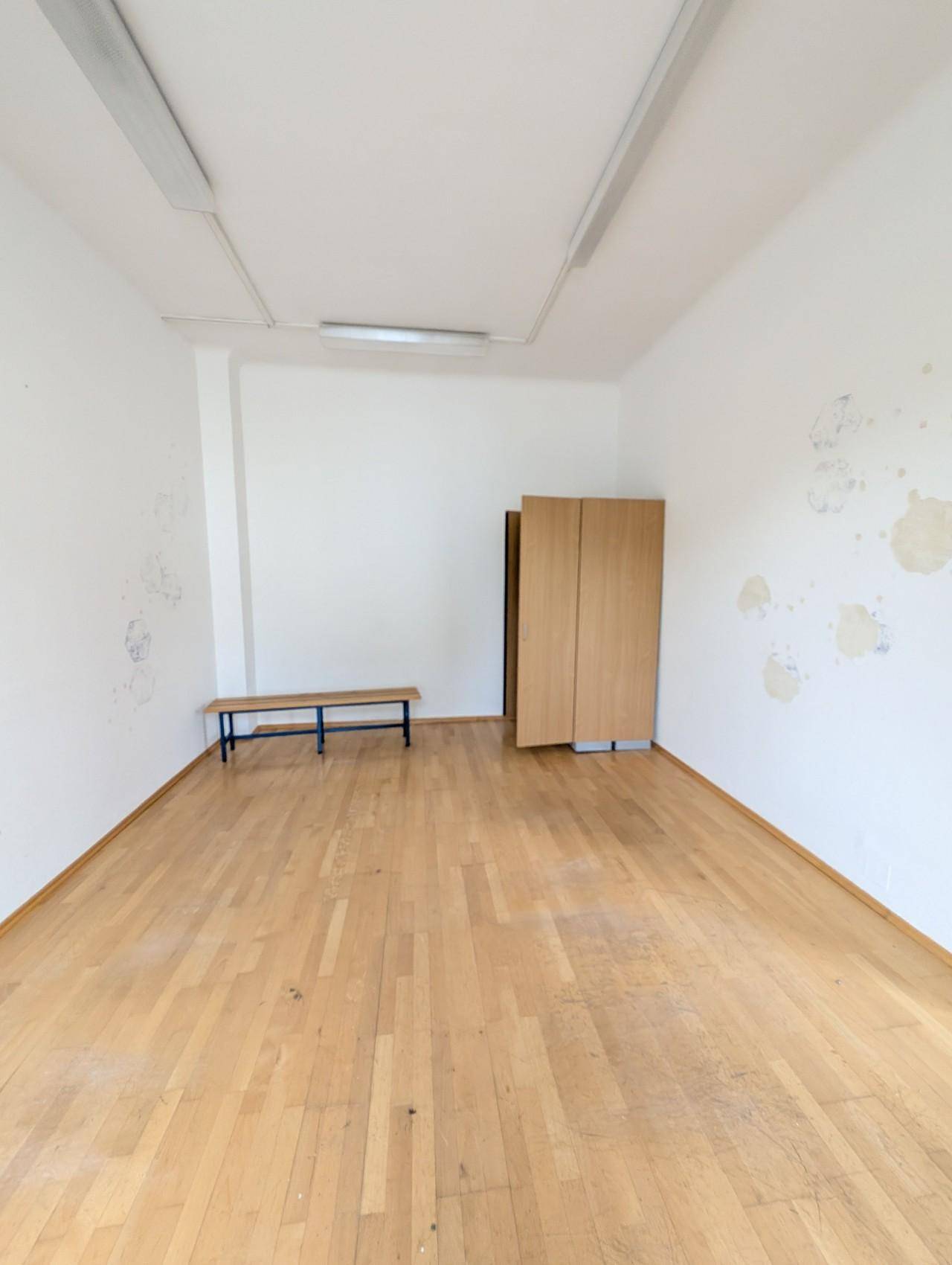 Heller Raum mit Holzboden, weißen Wänden und einem einfachen Holzschrank.