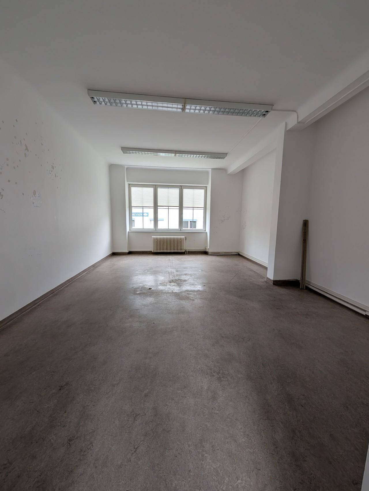 Leerer Raum mit weißen Wänden, einem Fenster und Heizkörper unter der Decke.