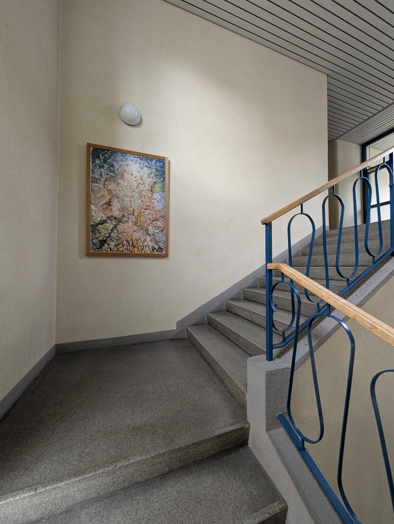 Treppenhaus mit Steinstufen, blauem Geländer und einem Bild an der hellen Wand.