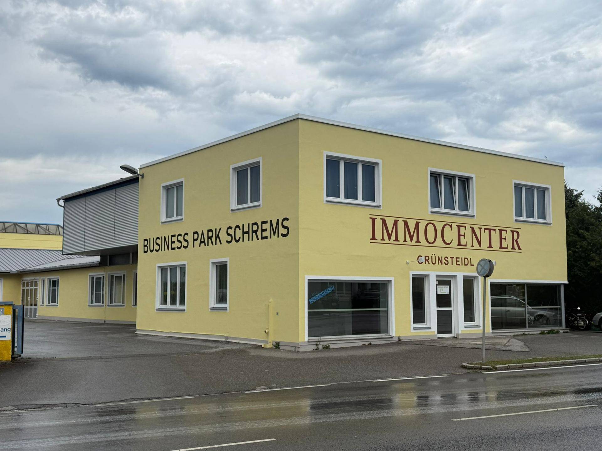 Seitenansicht des Gewerbegebäudes mit gelber Fassade und Beschriftungen für Business Park und Immocenter.