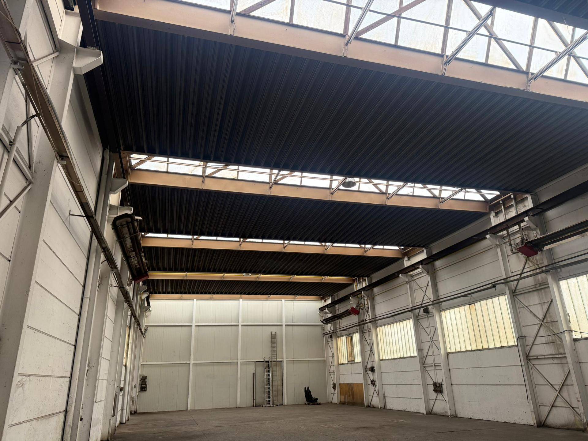 Blick auf die hohe Deckenkonstruktion einer Industriehalle mit Oberlichtern und Metallträgern.