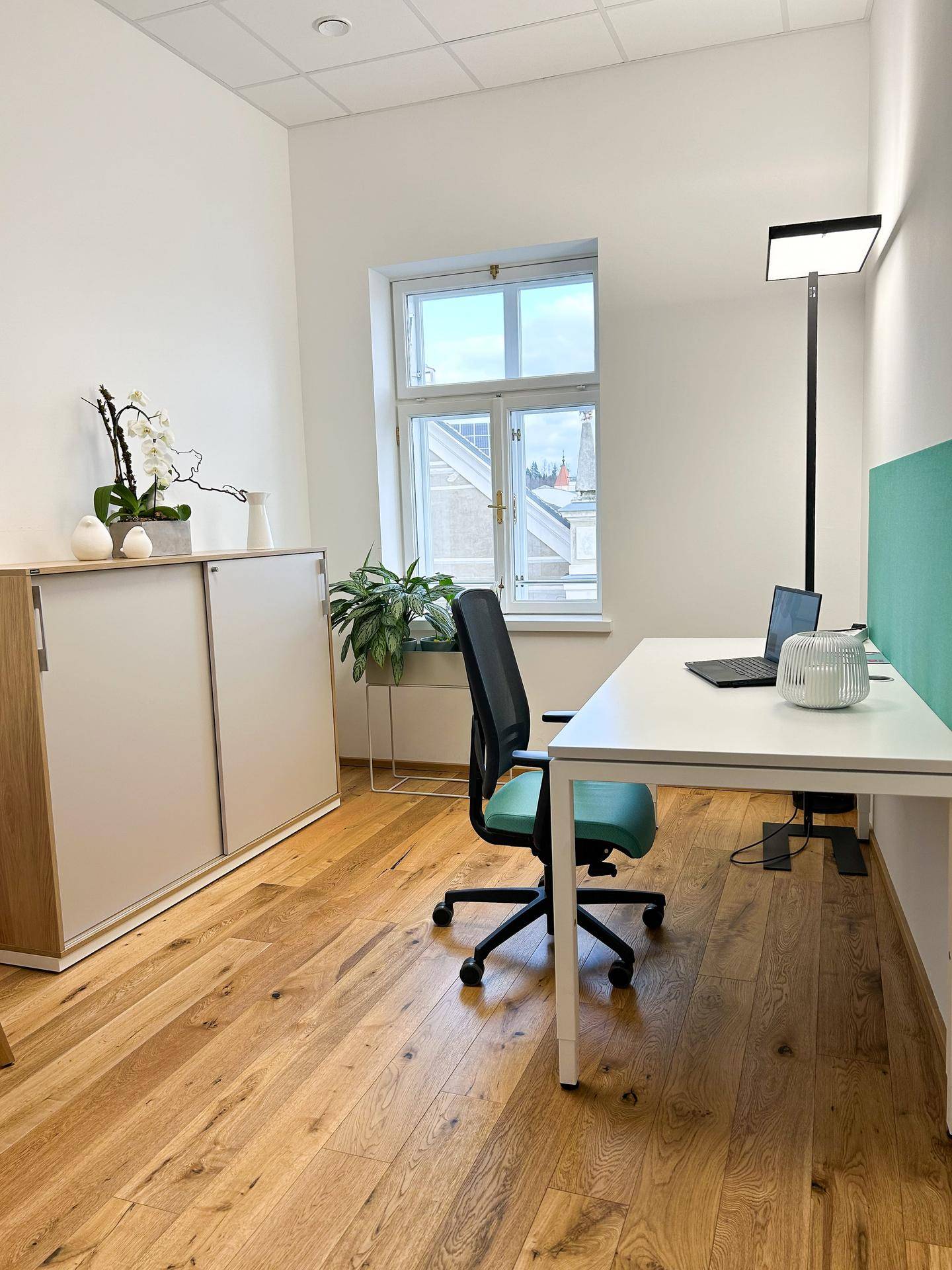 Modernes Büro mit Holzboden, einem Schreibtisch, Bürostuhl und einem Fenster mit Stadtblick.
