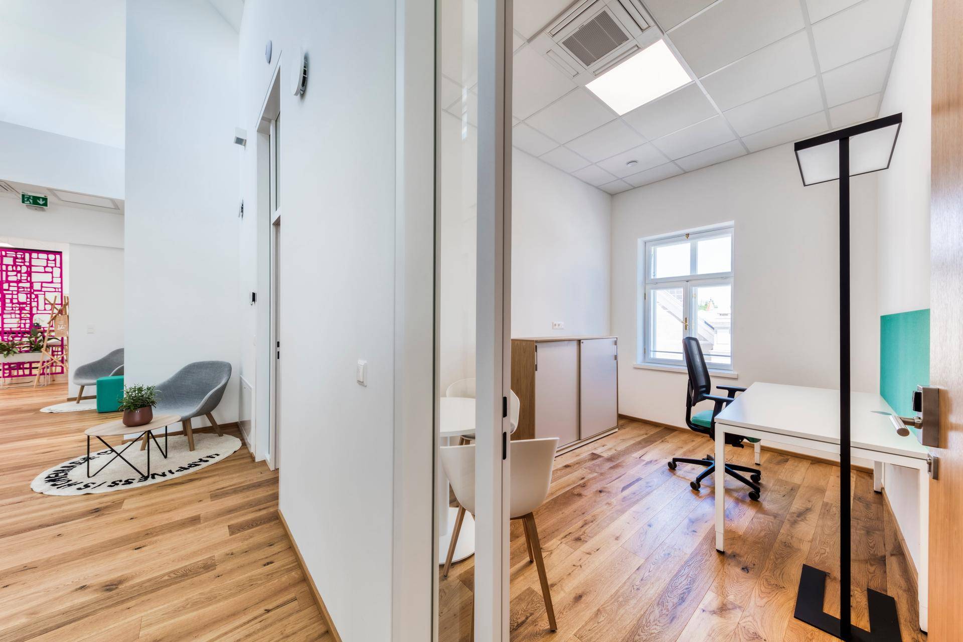 Moderner Bürobereich mit Holzboden, Glaswänden und Blick in ein weiteres Arbeitszimmer.
