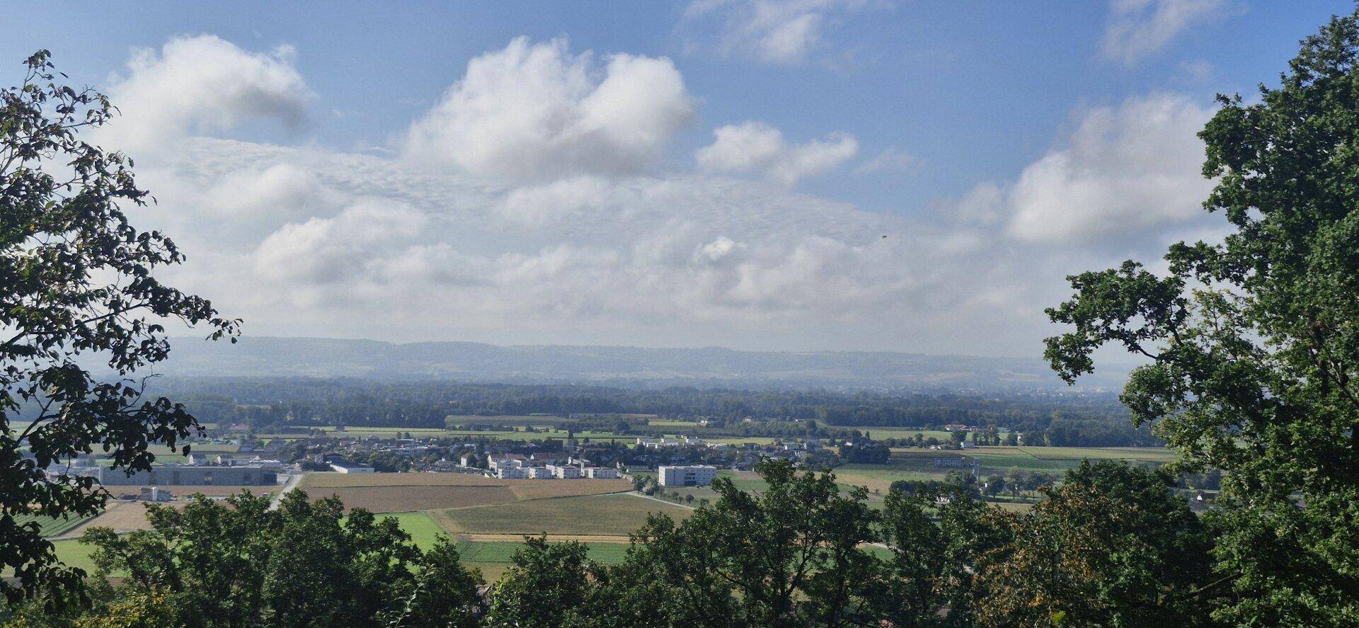 Panoramablick auf die weite Landschaft mit Siedlungen und Feldern unter einem bewölkten Himmel.