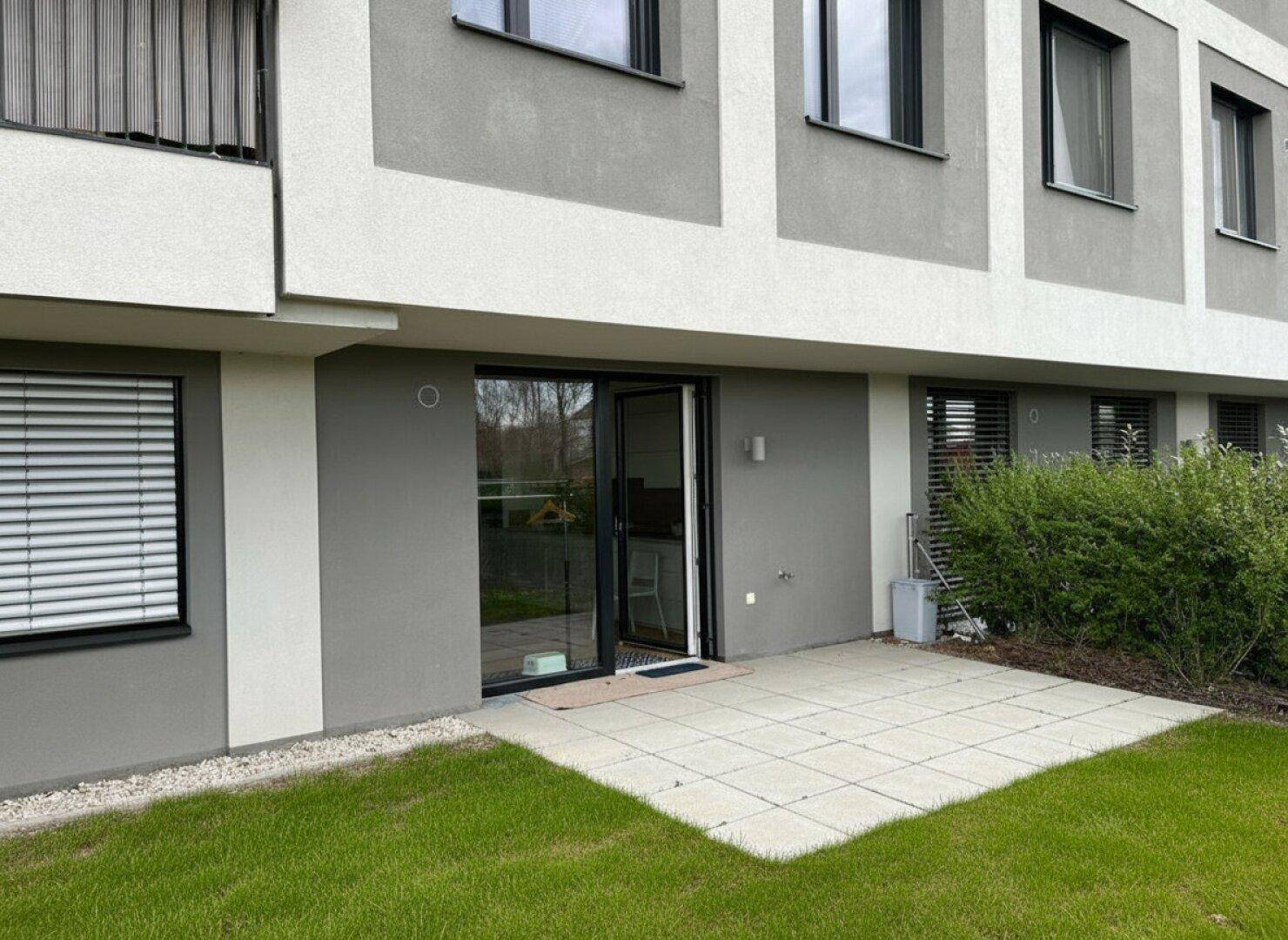 Außenansicht eines modernen Gebäudes mit ebenerdiger Terrasse und kleinem Rasenbereich.