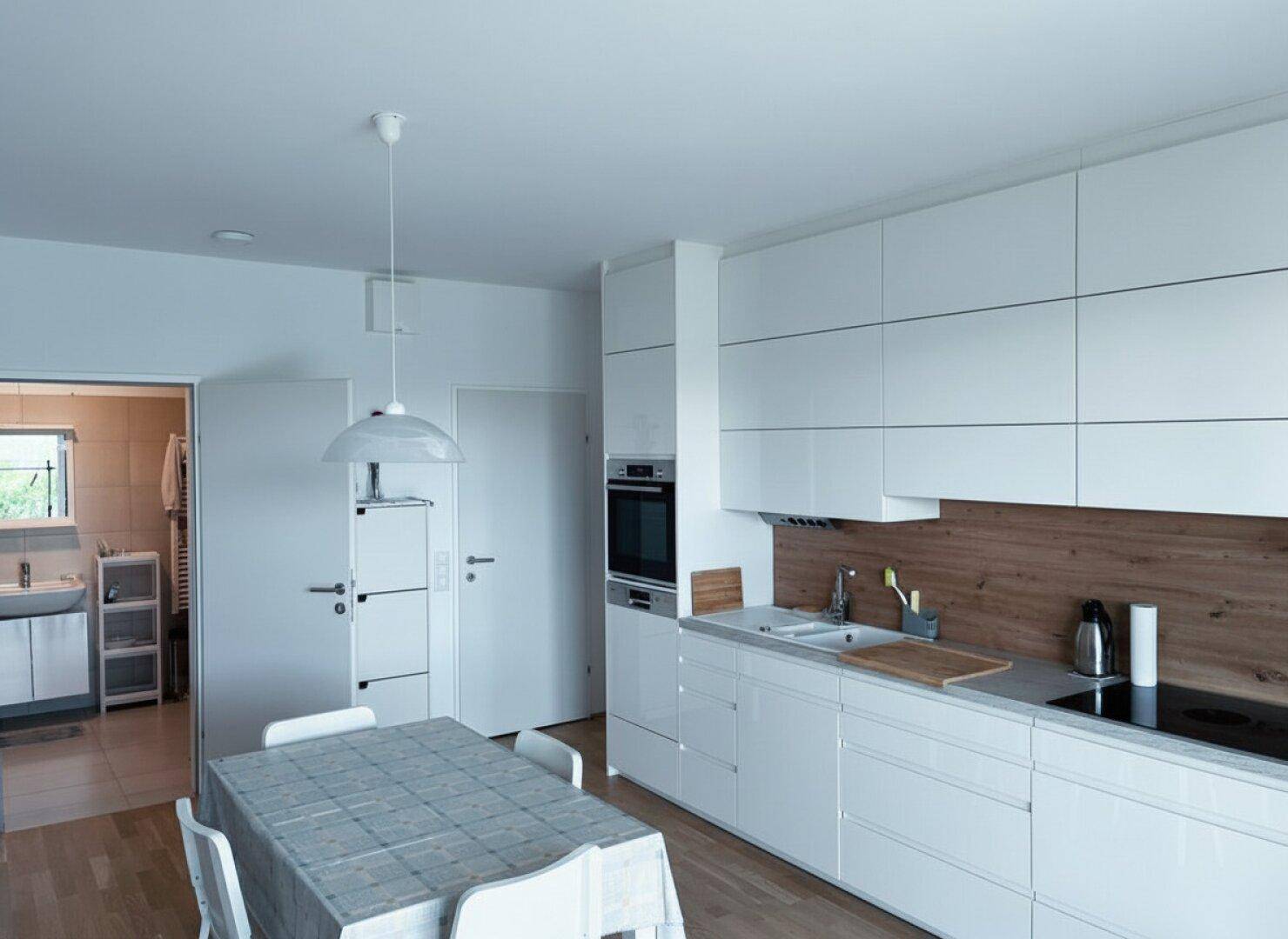 Helle, moderne Küche mit weißen Schränken, Holzarbeitsplatte und Essbereich, mit Blick in einen Nebenraum.
