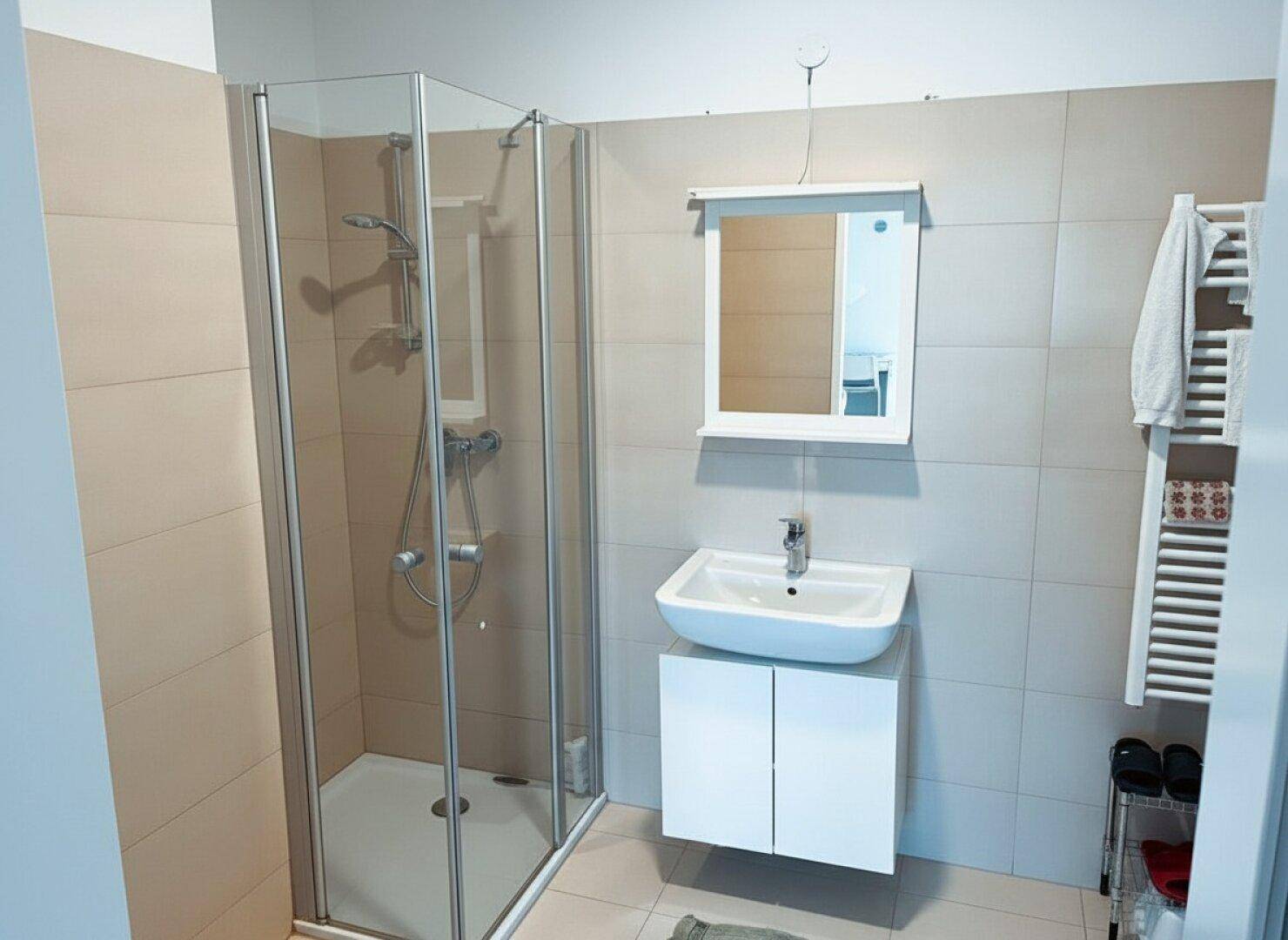 Helles Badezimmer mit moderner Duschkabine, Waschbecken und Handtuchheizkörper.