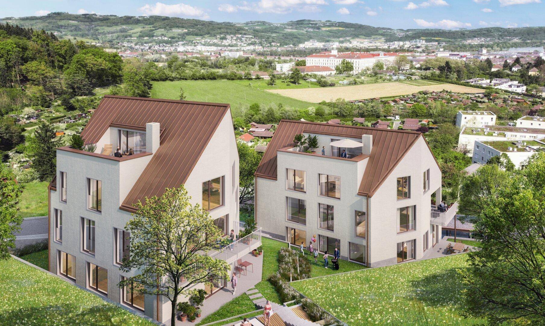Neubauten mit Satteldach und Dachterrassen, eingebettet in eine grüne Landschaft mit Fernblick auf die Stadt.