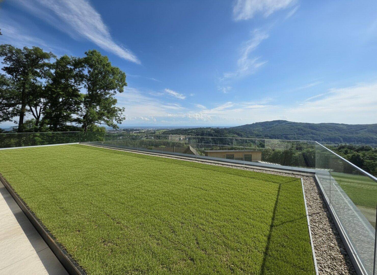 Weitläufige Terrassenfläche mit Kunstrasen und moderner Glasbrüstung, ideal für Entspannung im Freien.