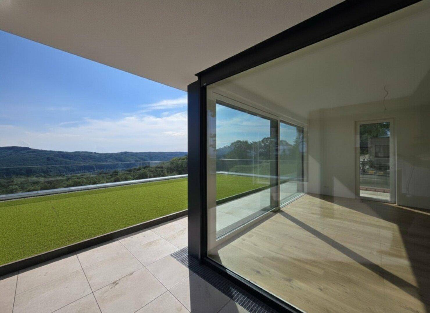 Heller Innenraum mit Holzboden und großen Schiebetüren, die auf eine Terrasse mit Weitblick führen.