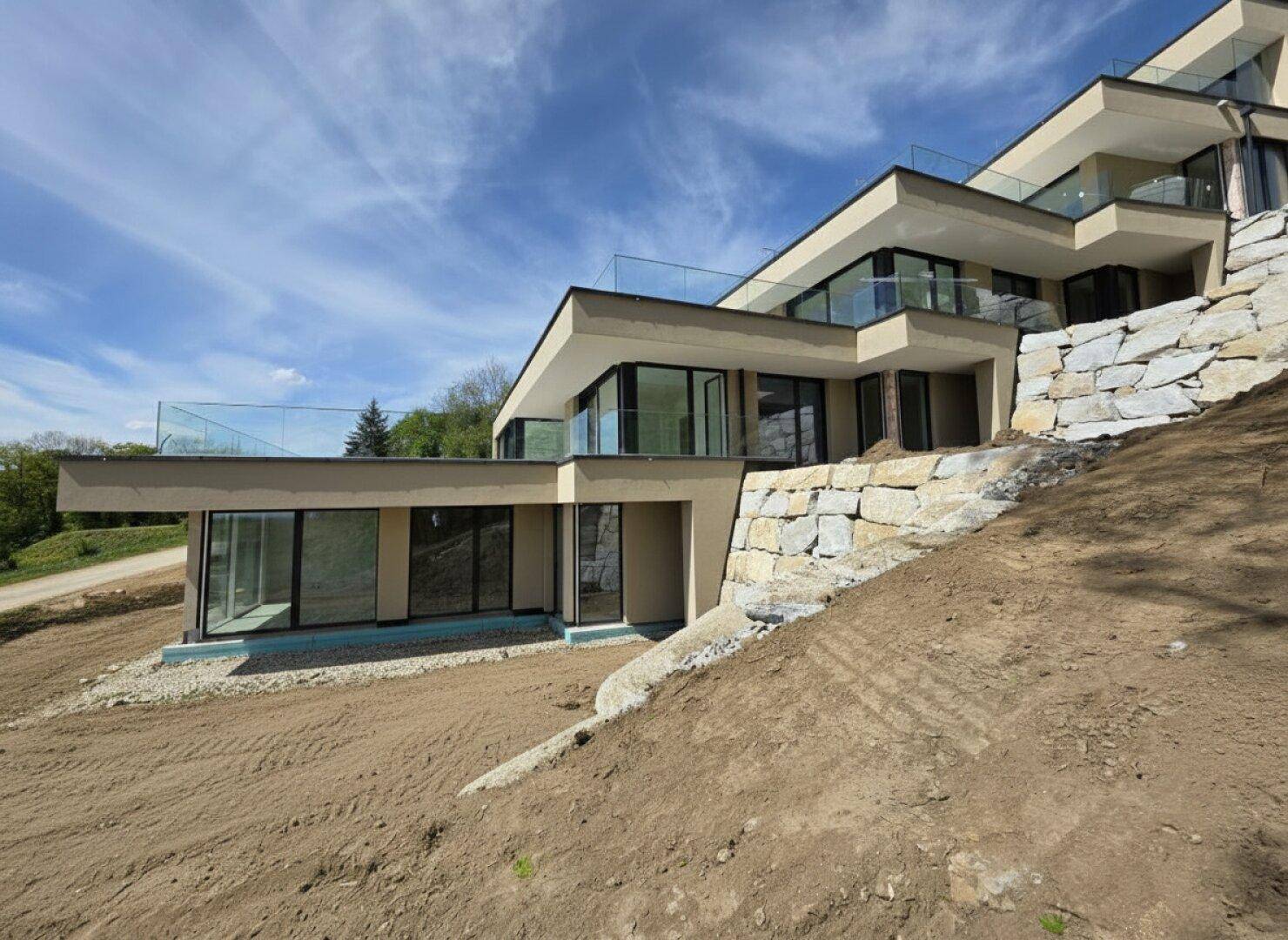 Modernes Terrassenhaus in Hanglage mit gestufter Architektur und Natursteinmauern im Bau.