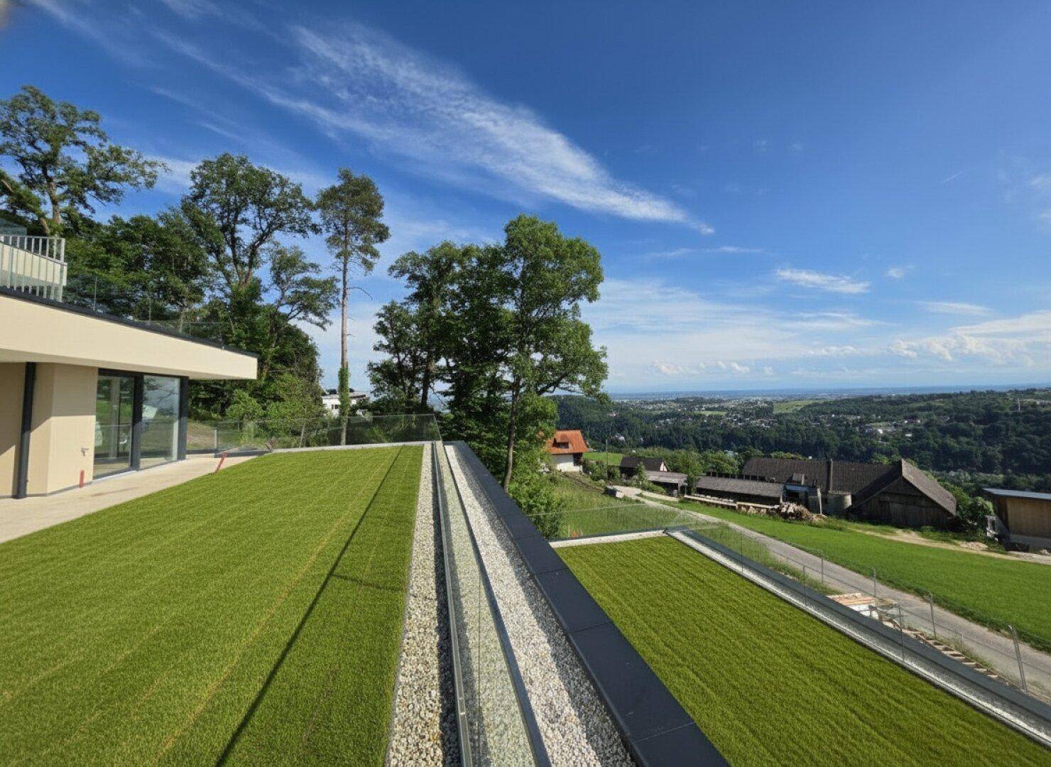 Weitläufige Terrassenfläche mit Kunstrasen und Panoramablick auf die umliegende Landschaft und Stadt.