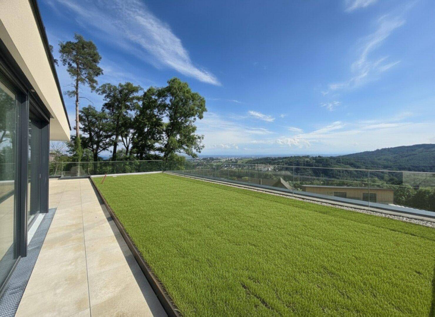 Großzügige Terrasse mit Kunstrasen und moderner Glasbrüstung, bietet einen weiten Blick in die Ferne.