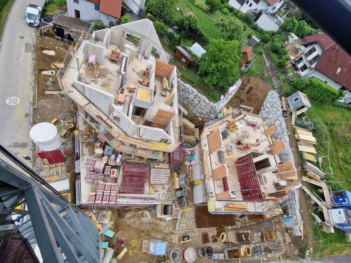 Luftaufnahme von zwei im Bau befindlichen Gebäuden mit unregelmäßigen Formen und Baumaterialien.