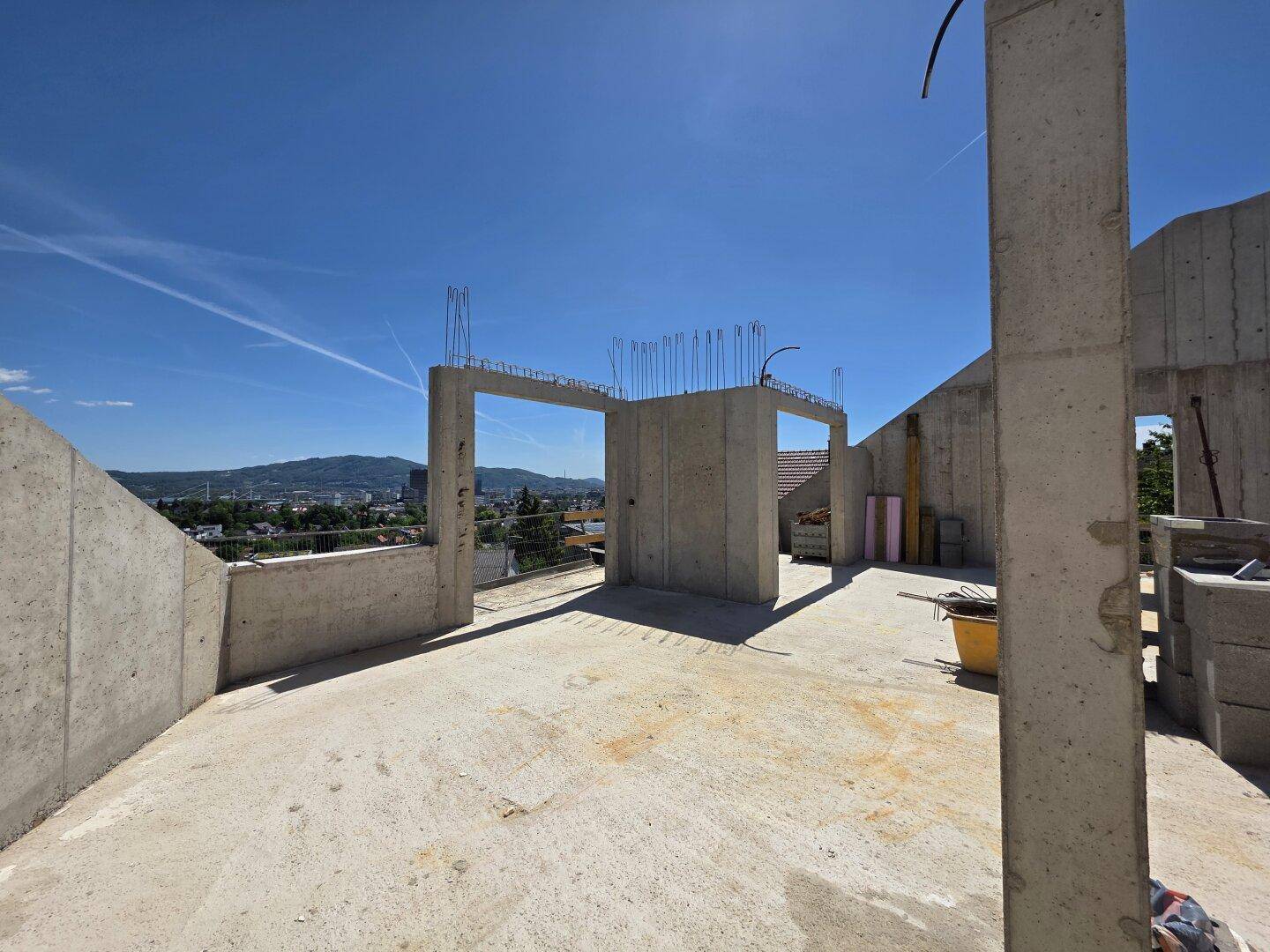 Unfertiger Innenraum mit Betonwänden und weitem Blick auf die Stadt und die umliegende Landschaft.
