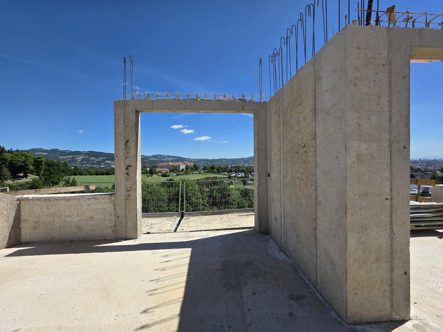 Aussicht von der Baustelle auf die weite grüne Landschaft und die historischen Gebäude in der Ferne.