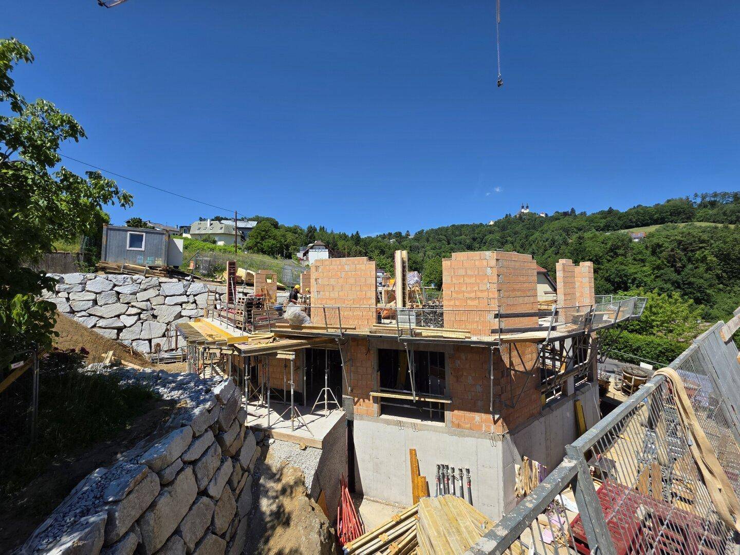 Das im Bau befindliche Gebäude mit Ziegelwänden und Betonstrukturen, umgeben von grünen Hügeln.