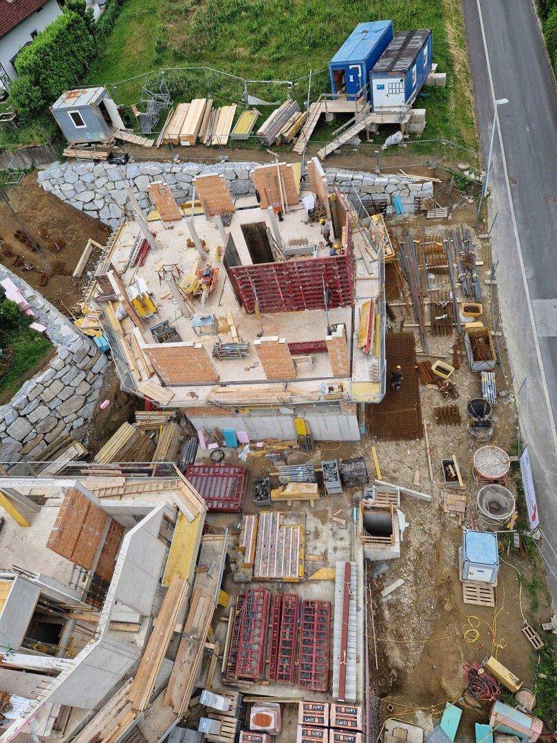 Überblick über die Baustelle mit einem im Bau befindlichen Gebäude und zahlreichen Baumaterialien.