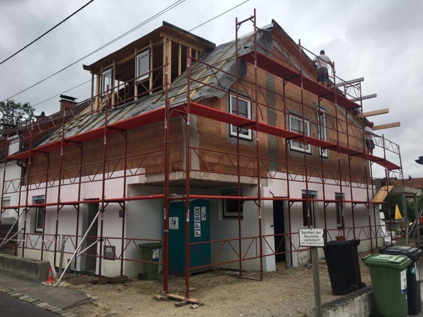 Haus im Bau mit vollständigem Gerüst und sichtbaren Ziegelwänden, ein Arbeiter auf dem Dach.