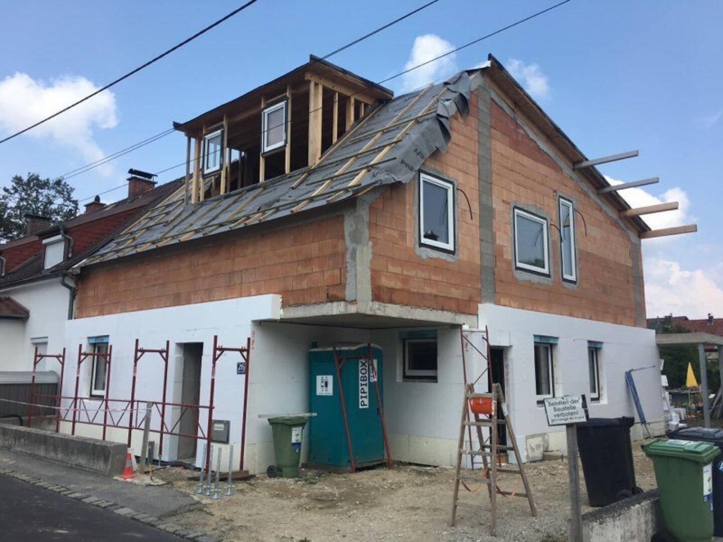 Haus im Bauzustand mit sichtbarer Ziegelmauer und Dachkonstruktion, bereit für weitere Arbeiten.