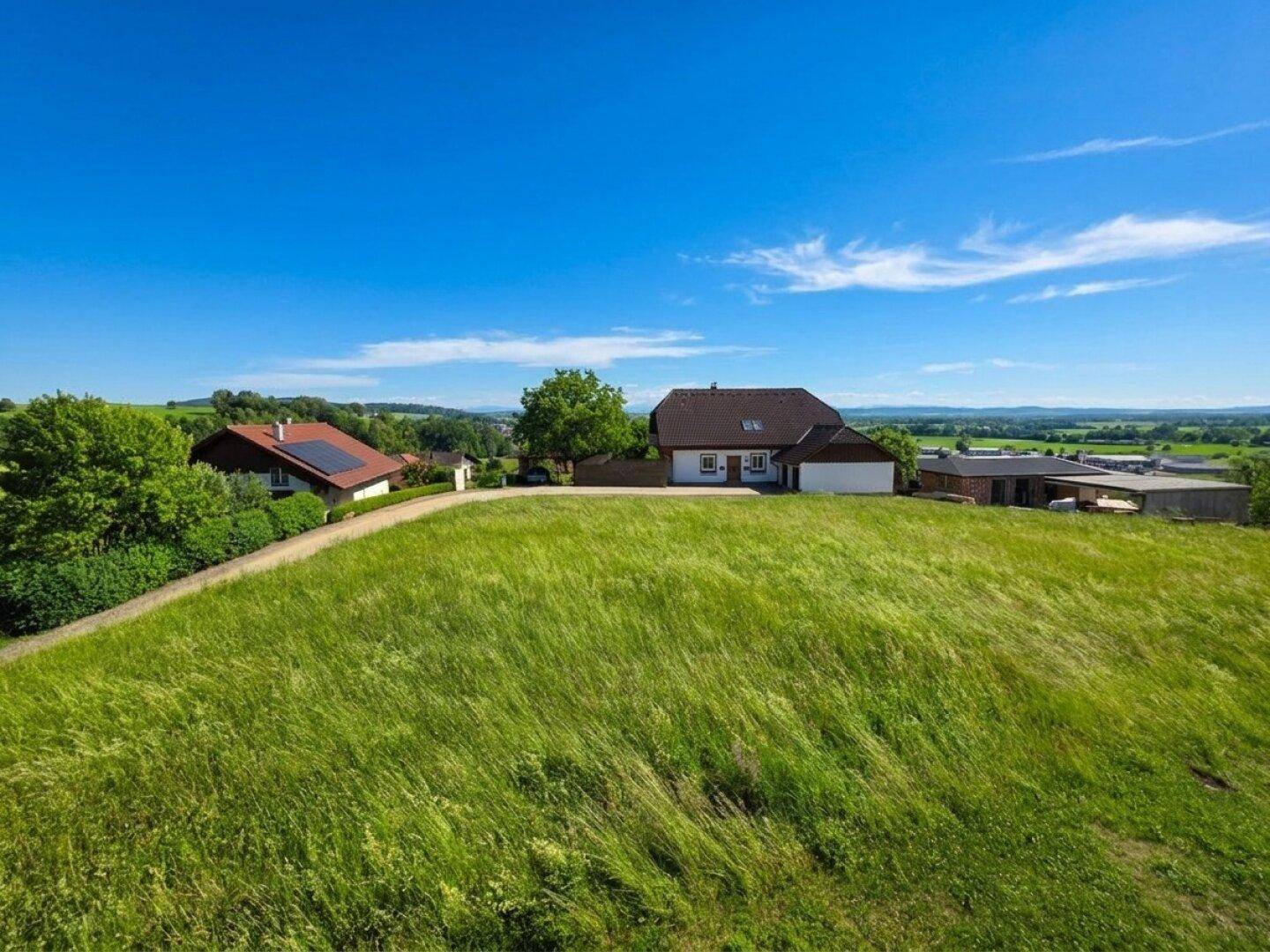 Haus auf einem sonnigen Hügel mit weitem Blick über die grüne Landschaft und blauen Himmel.