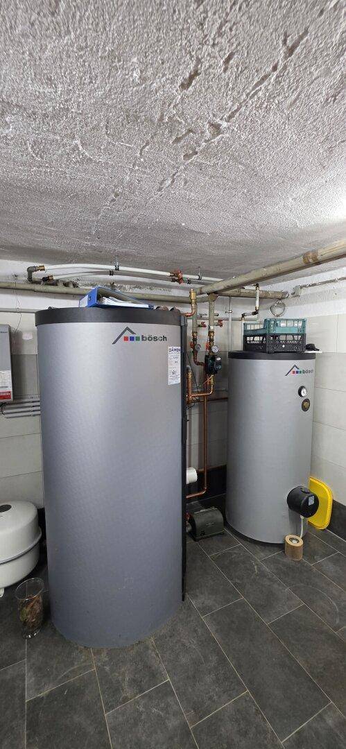 Heizungsraum im Keller mit zwei großen Warmwasserspeichern und technischen Installationen.