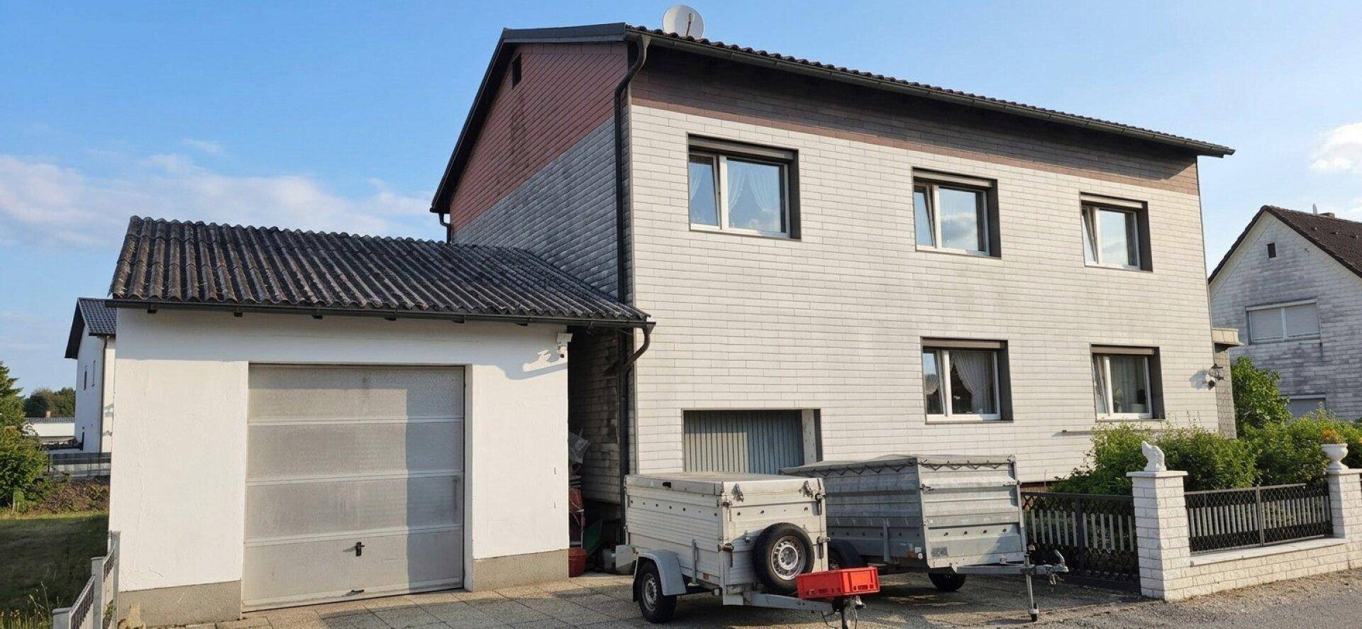 Hausfassade mit integrierter Garage und gepflasterter Einfahrt.