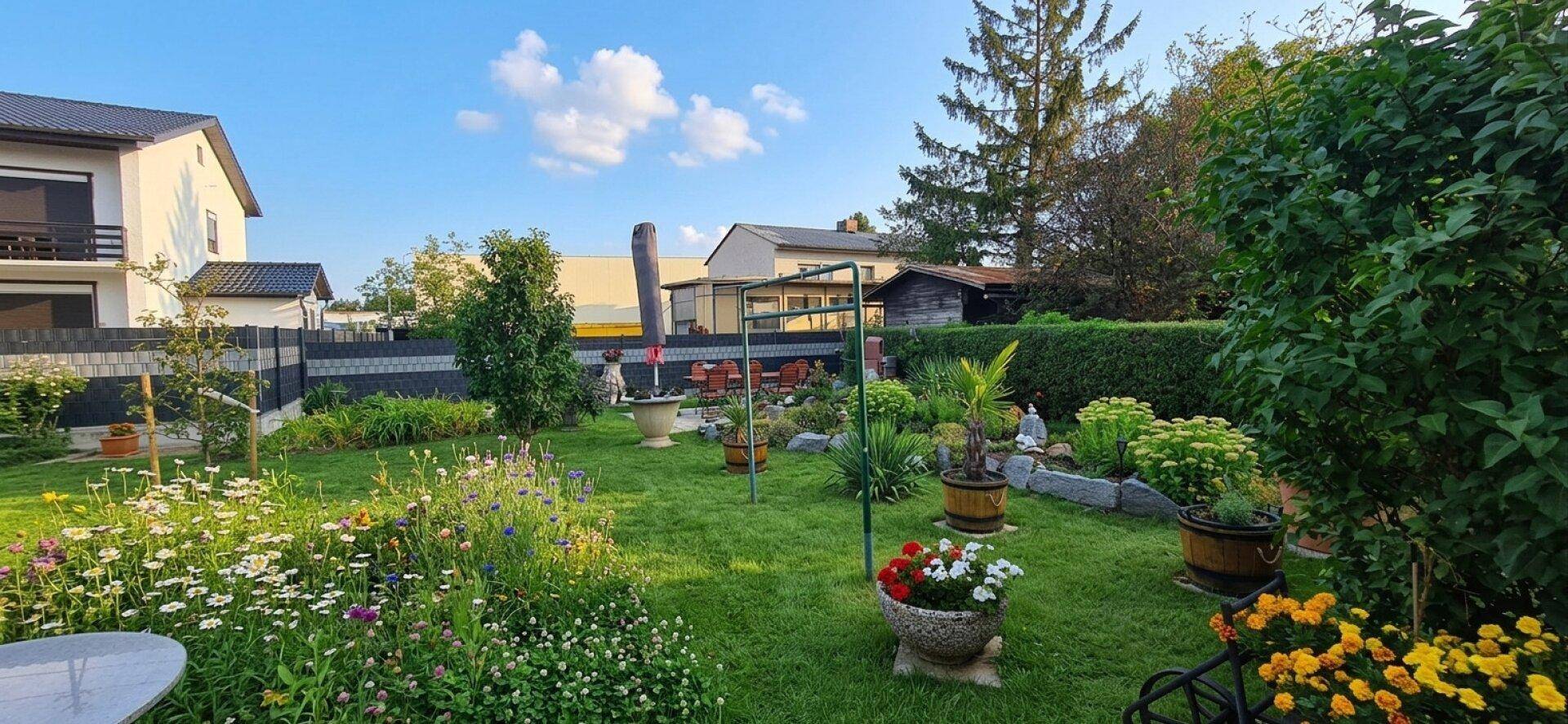 Gepflegter Garten mit weitläufiger Rasenfläche, bunten Blumenbeeten und verschiedenen Pflanzen.