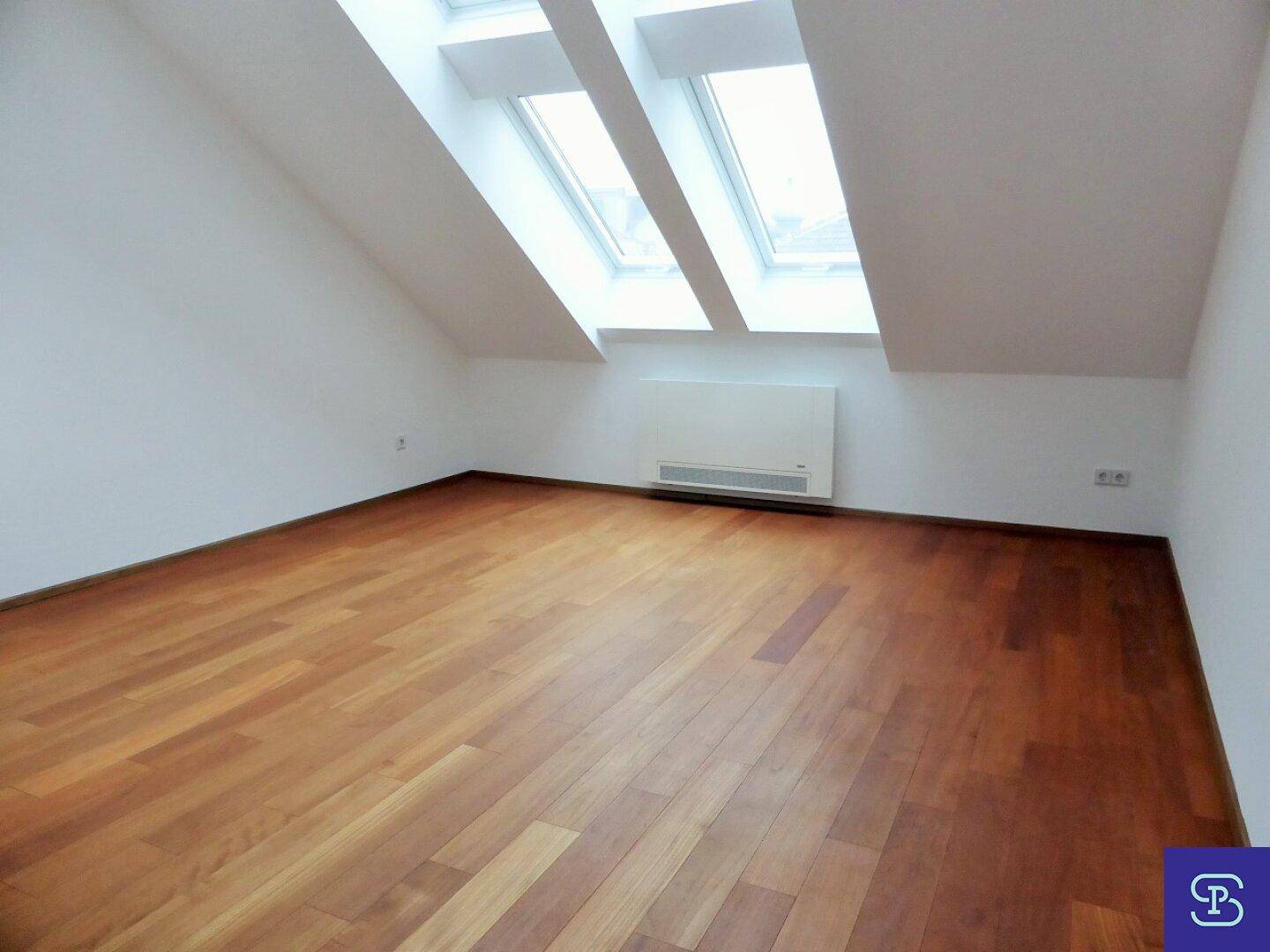 Helles Zimmer mit Holzboden, Dachschrägen und großen Dachfenstern.