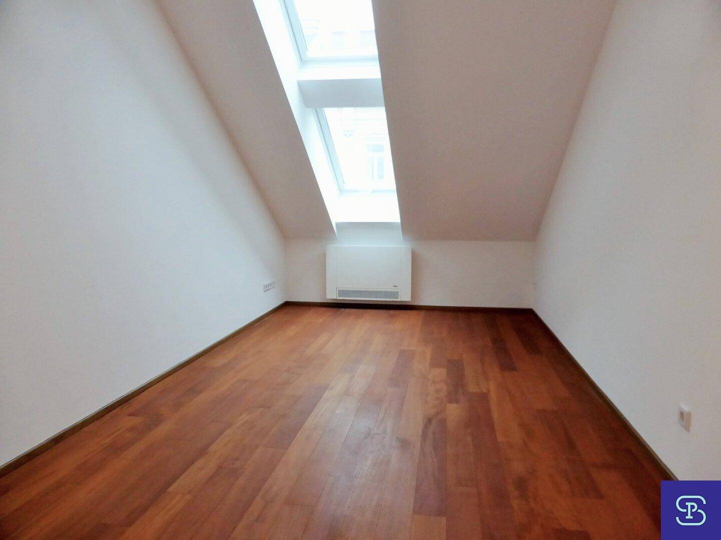Helles Zimmer mit Holzboden, Dachschräge und einem großen Dachfenster.