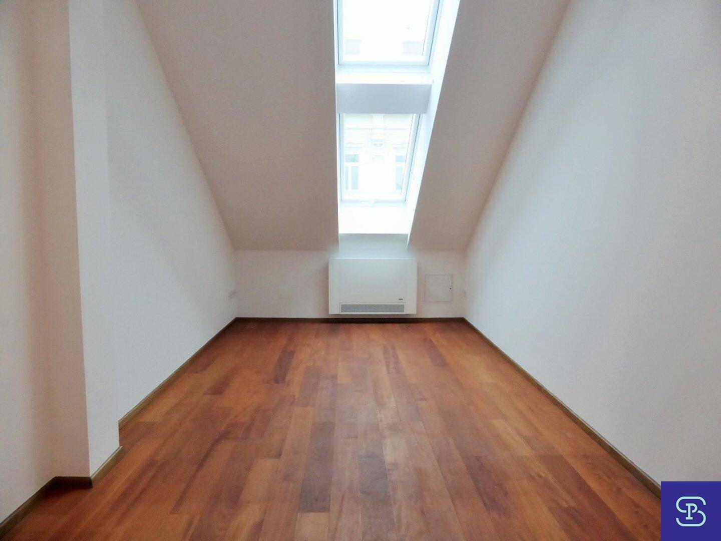 Helles Zimmer mit Holzboden, Dachschräge und einem großen Dachfenster.