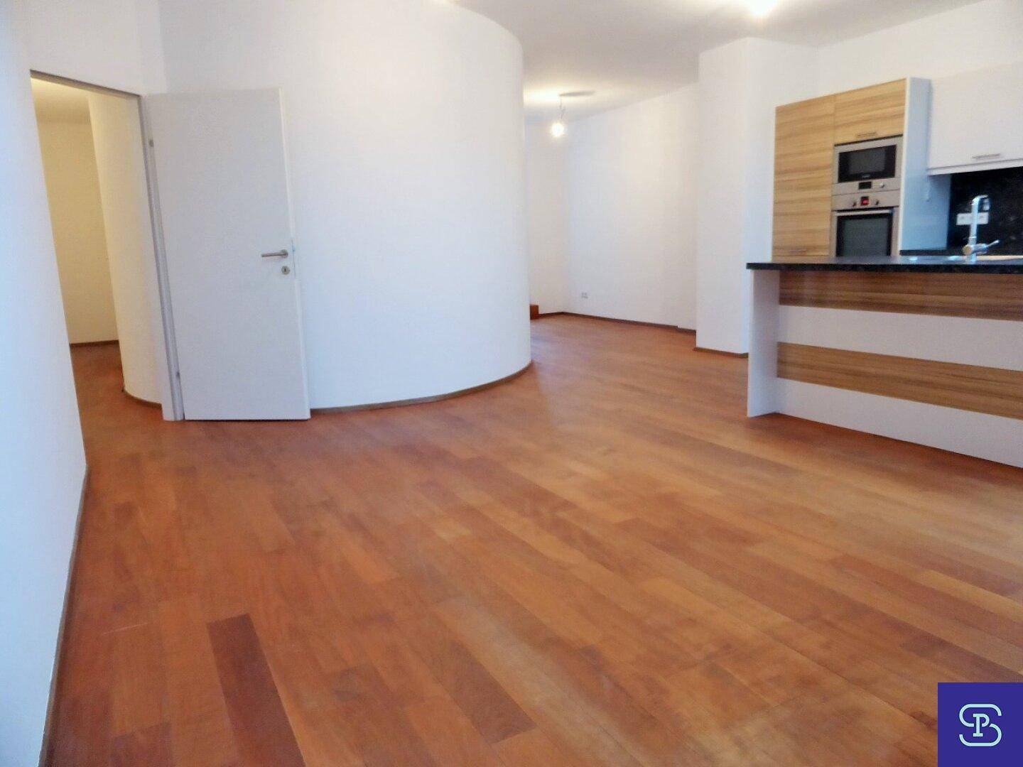 Geräumiger offener Wohnbereich mit Holzboden und moderner Küchenzeile.