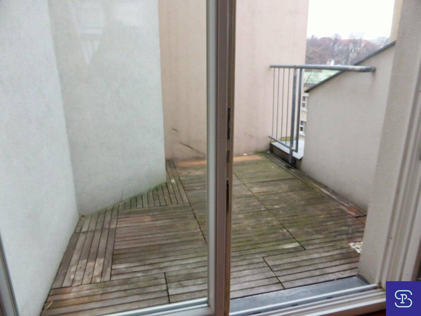 Kleiner Balkon mit Holzfliesen und Metallgeländer, ideal für Entspannung.