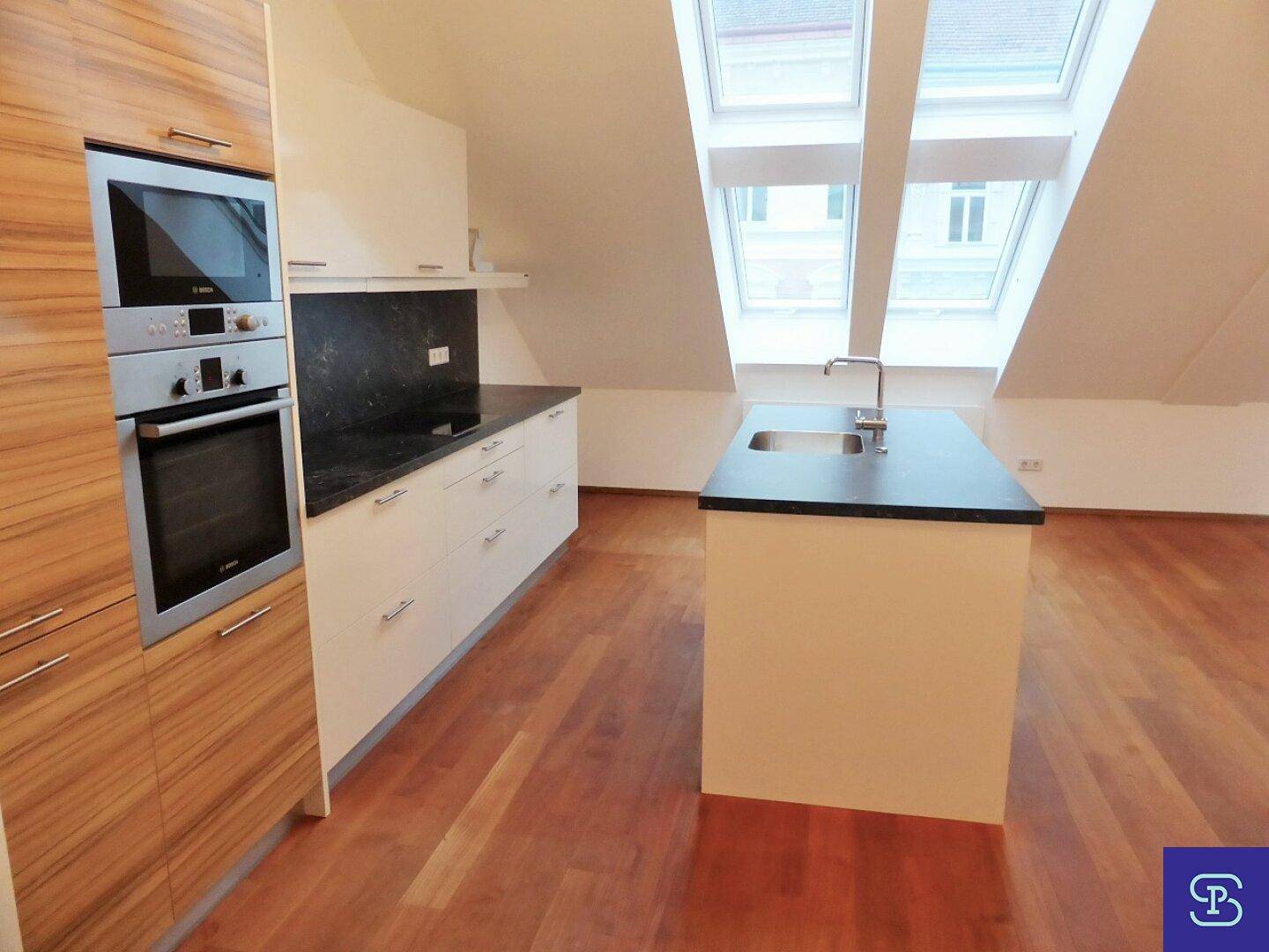 Moderne Einbauküche mit Kochinsel, dunkler Arbeitsplatte und Dachfenstern.