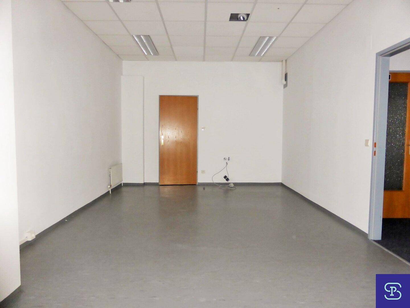 Leerer Büroraum mit grauem Boden, weißen Wänden und einer Holztür, bereit zur individuellen Gestaltung.