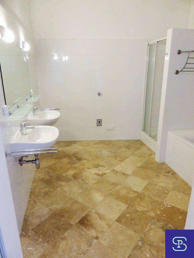 Geräumiges Badezimmer mit zwei Waschbecken, Duschkabine und Fliesenboden in hellen Farbtönen.