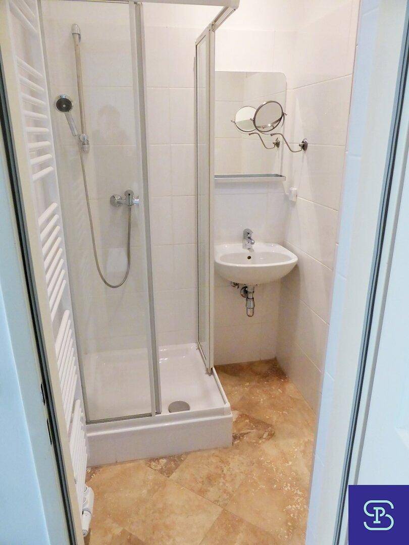 Kleines Badezimmer mit Duschkabine, Waschbecken und Spiegel, ausgestattet mit Fliesenboden.