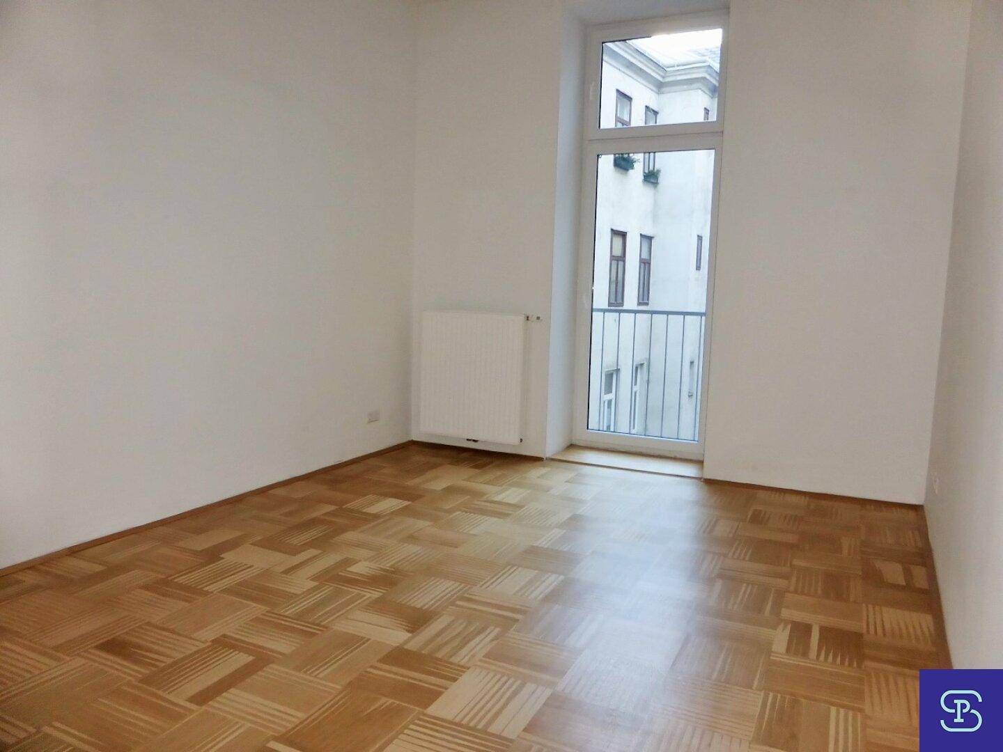 Helles Zimmer mit Parkettboden und einem französischen Balkon, der frische Luft hereinlässt.