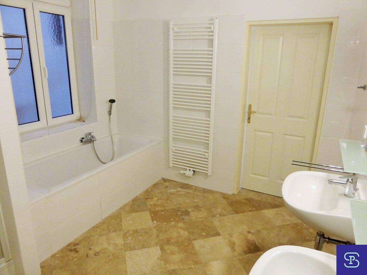 Badezimmer mit Badewanne, Bidet, Waschbecken und beheiztem Handtuchhalter auf Fliesenboden.