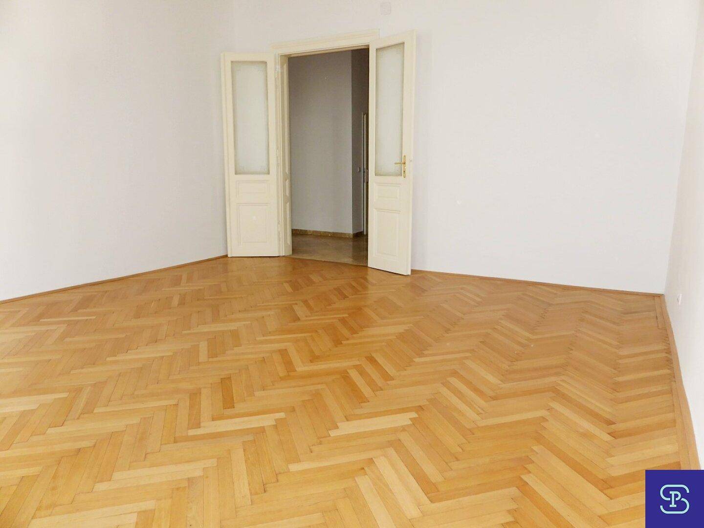 Heller Raum mit Fischgrätparkett und Doppeltüren, die zu einem weiteren Zimmer führen.