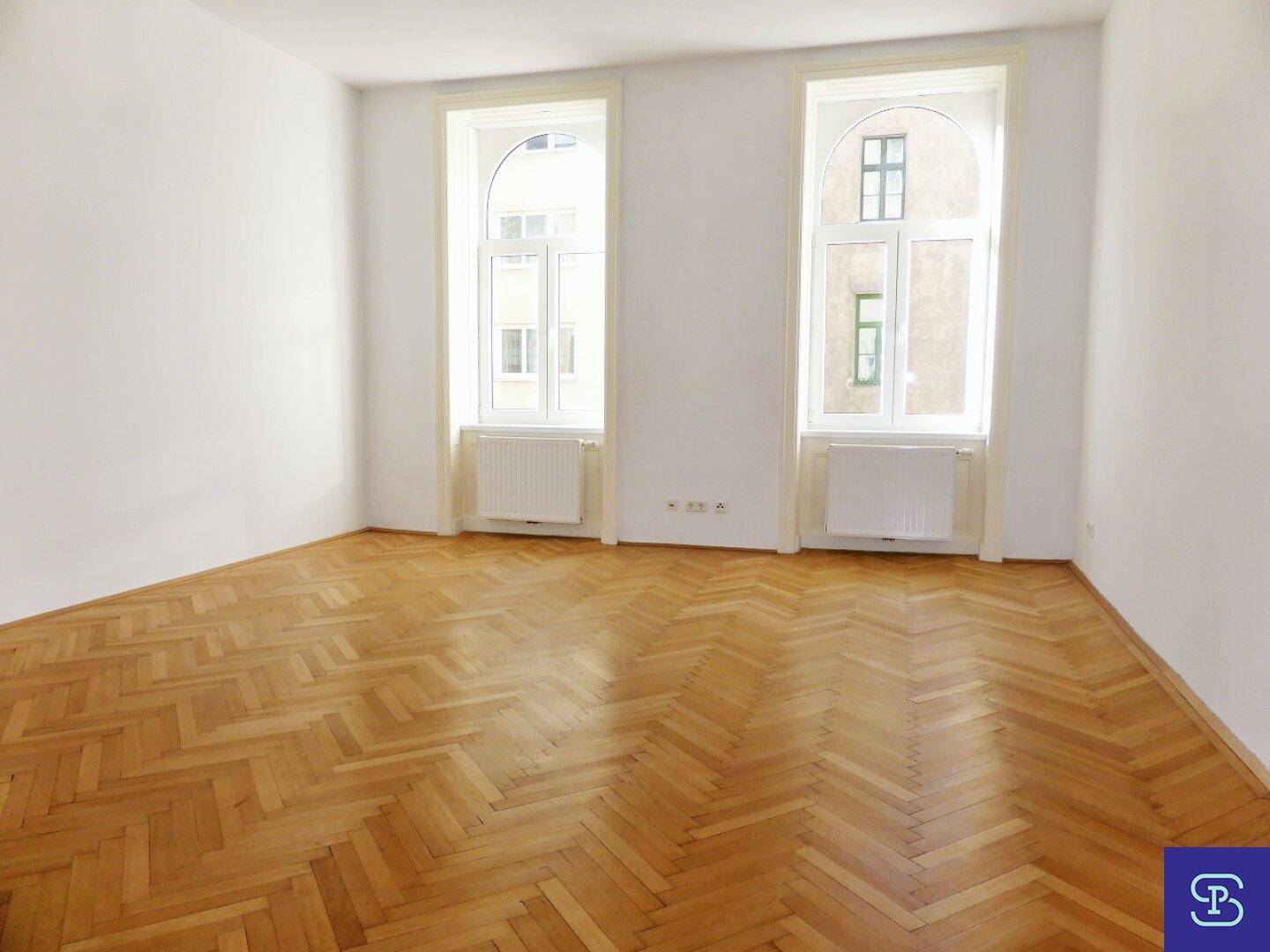 Geräumiges Zimmer mit Fischgrätparkett und hohen Bogenfenstern, die den Raum mit Tageslicht füllen.