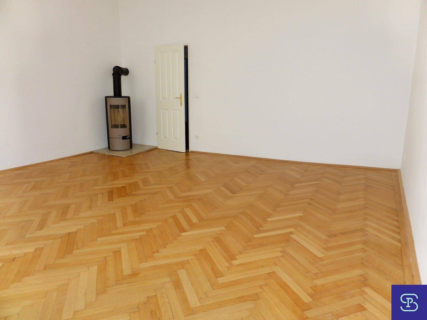 Helles Zimmer mit Fischgrätparkett und einem modernen Holzofen, der für zusätzliche Wärme sorgt.