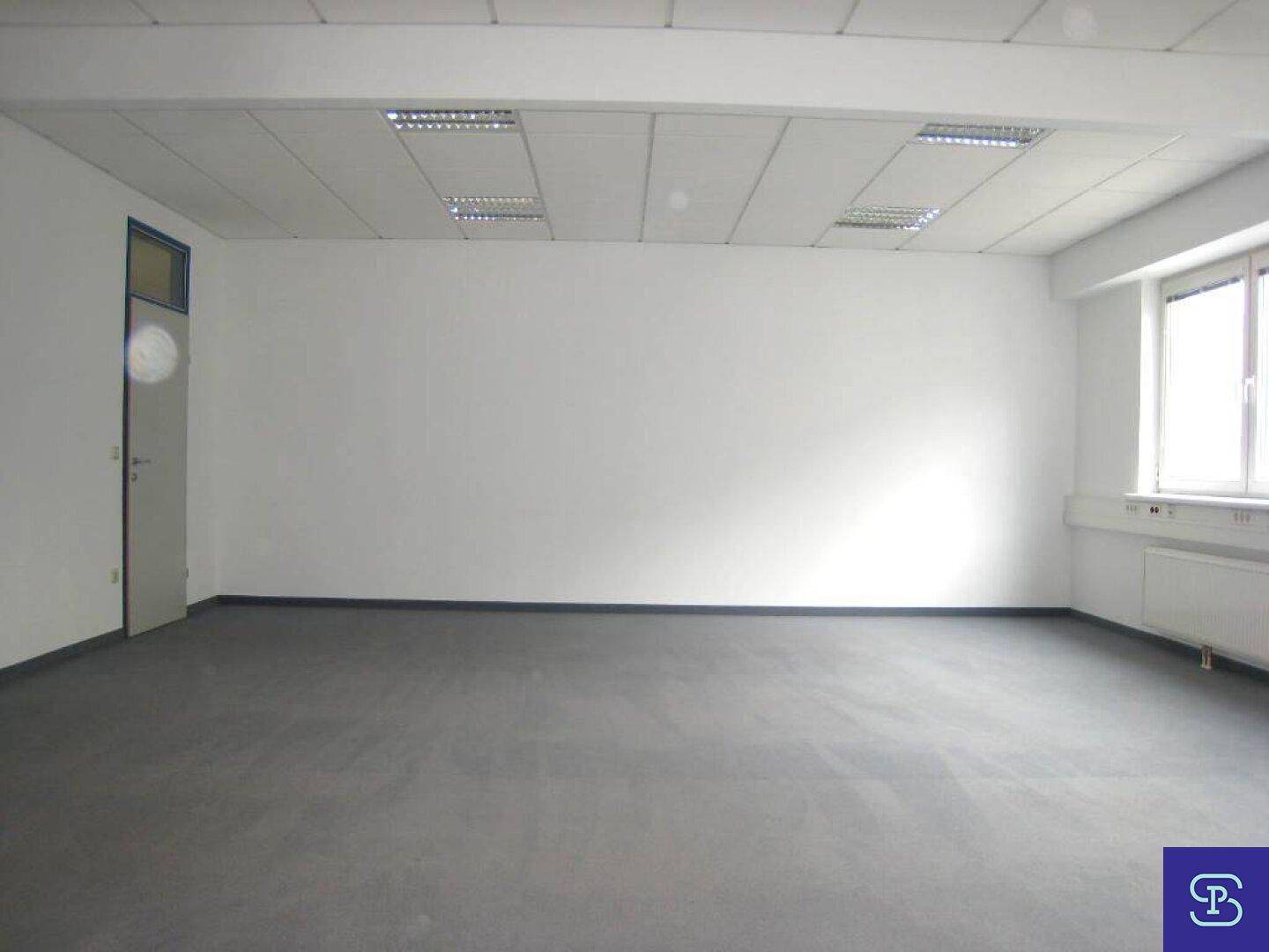 Helles Büro mit Teppichboden und einer Tür, die zu einem weiteren Bereich führt, ideal für flexible Nutzung.