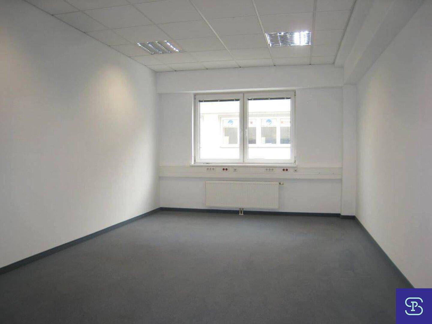 Büro mit Teppichboden und einem breiten Fenster, das viel natürliches Licht in den Raum bringt, mit Heizkörper.