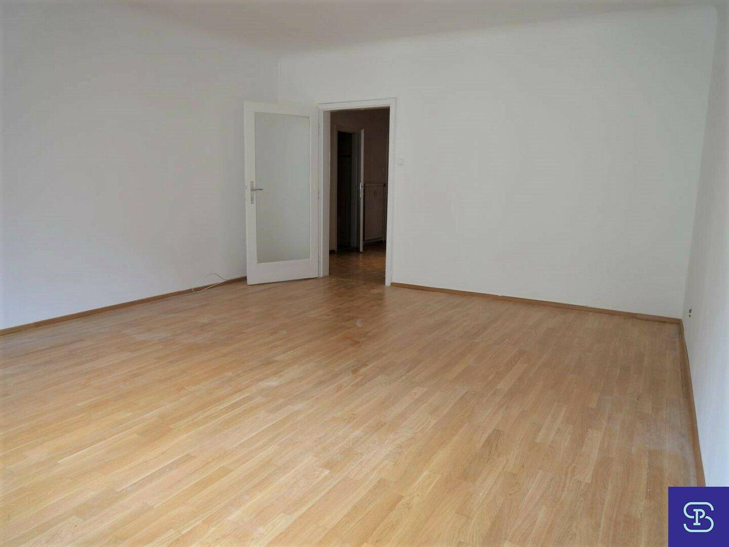 Geräumiges, leeres Zimmer mit Parkettboden und Zugang zu einem weiteren Raum.
