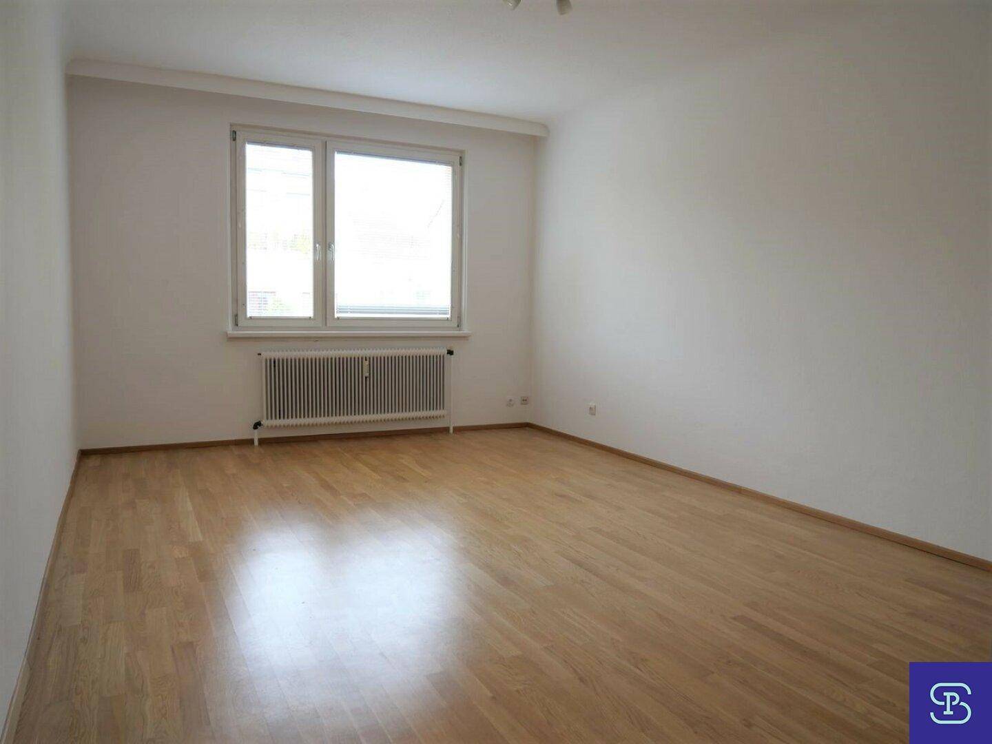 Lichtdurchflutetes Zimmer mit Parkettboden und Heizkörper unter dem Fenster.