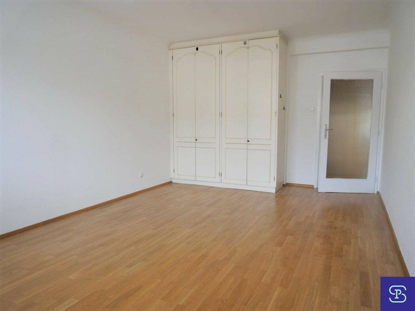 Helles Zimmer mit Parkettboden, Einbauschrank und einer Tür mit Glaseinsatz.