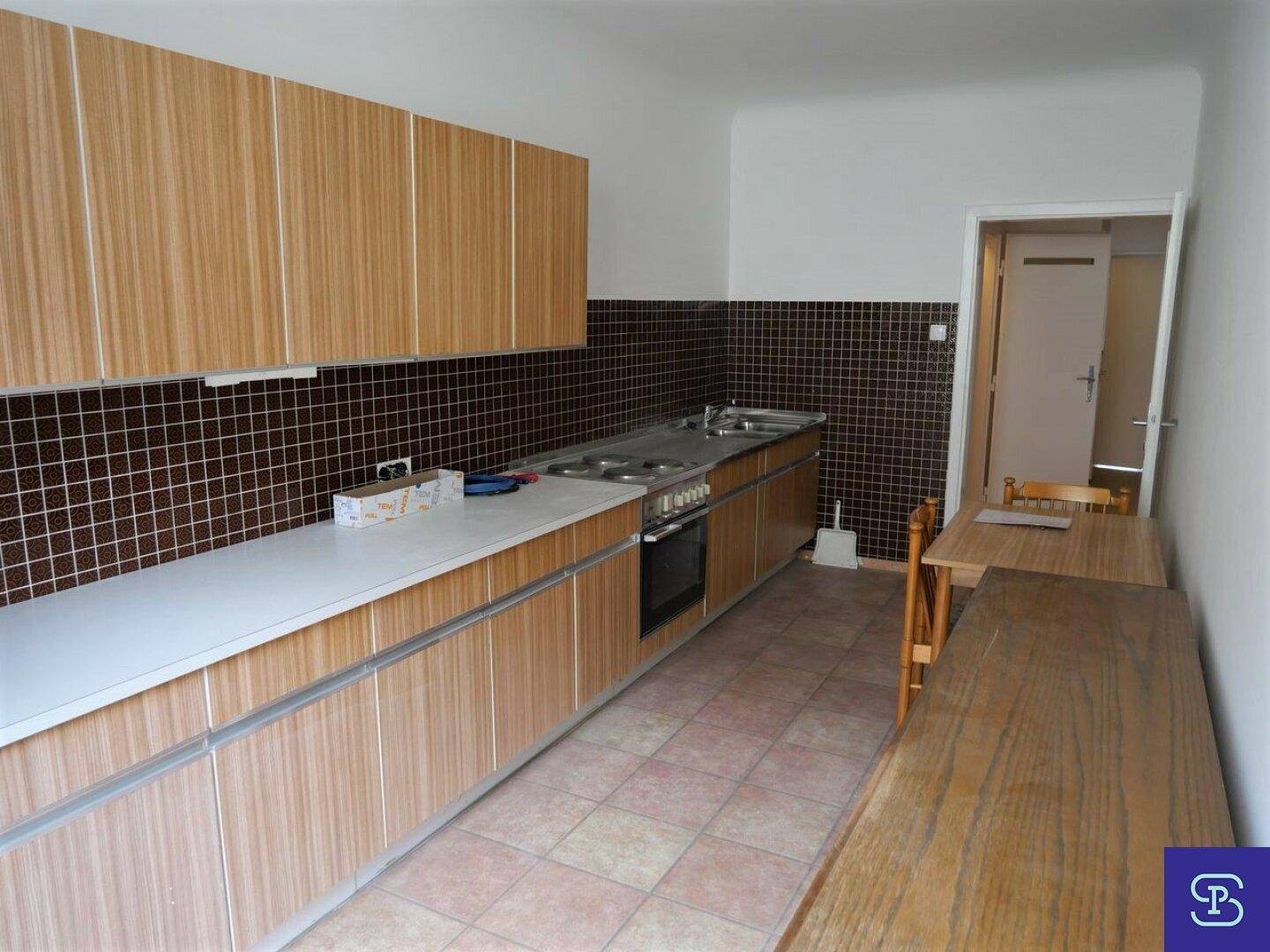 Längliche Küche mit Holzschränken, braunen Fliesen und Essbereich.