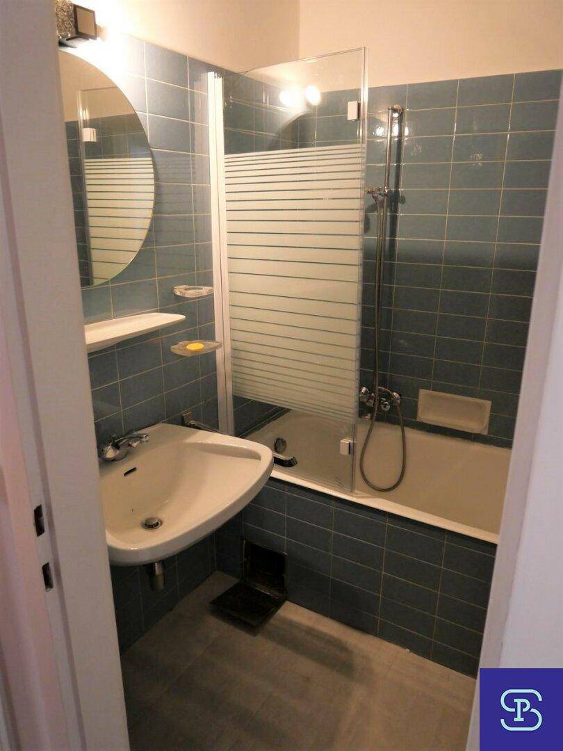 Badezimmer mit blauen Fliesen, Badewanne mit Duschwand und Waschbecken.
