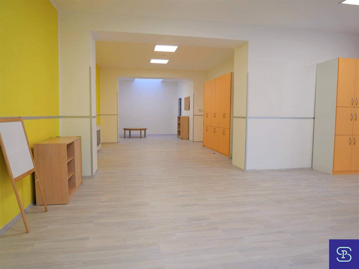 Langer Flur mit hellem Laminatboden, gelben Akzentwänden und orangefarbenen Schließfächern für Kinder.